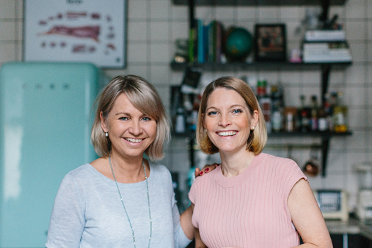 Sofia Antonsson and Jeanette Steijer smiling in a kitchen with a vintage refrigerator and shelving in the background.