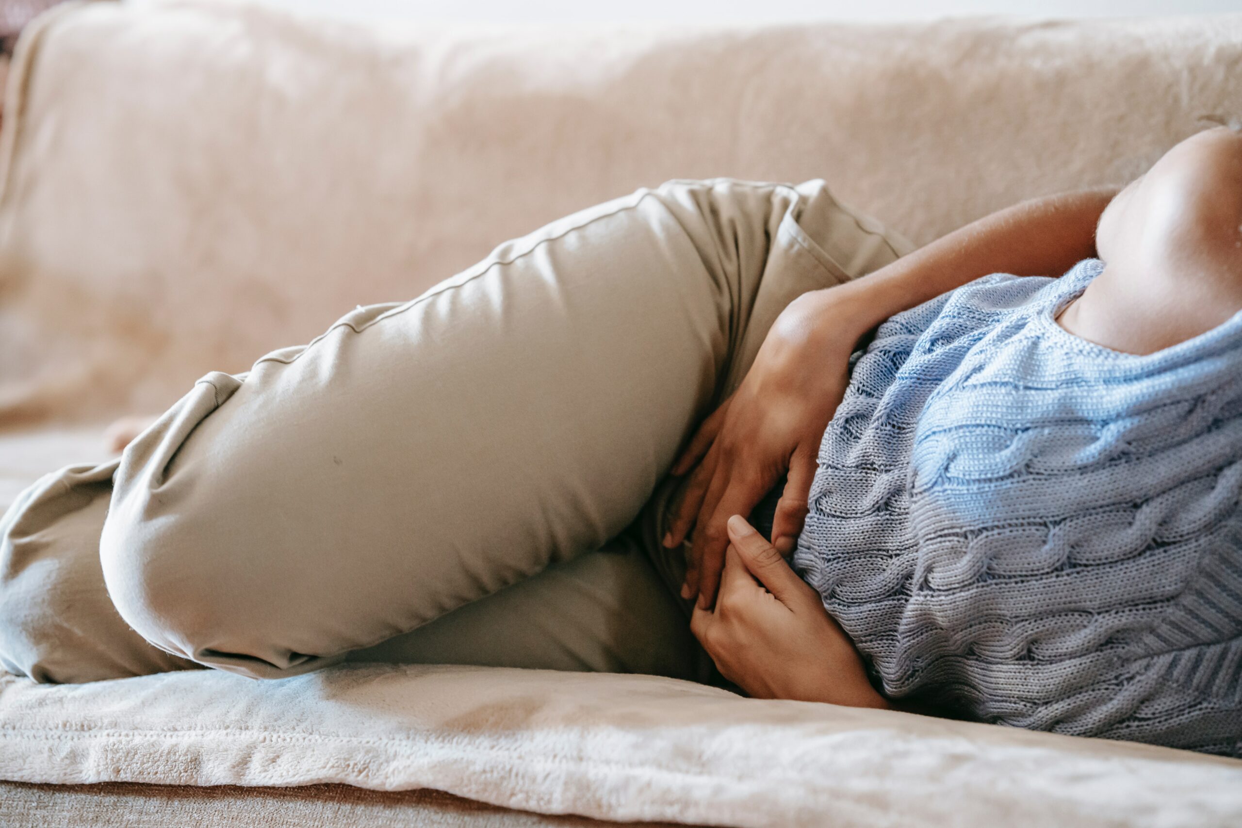 A person lying on their side on a couch, holding their abdomen, potentially experiencing discomfort or pain.