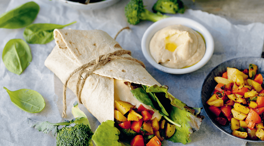 A healthy wrap tied with twine, filled with leafy greens and colorful grilled vegetables, accompanied by hummus and a side of diced seasoned vegetables.